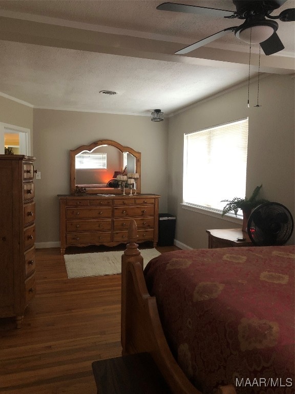 bedroom with a textured ceiling, crown molding, dark wood-type flooring, and ceiling fan