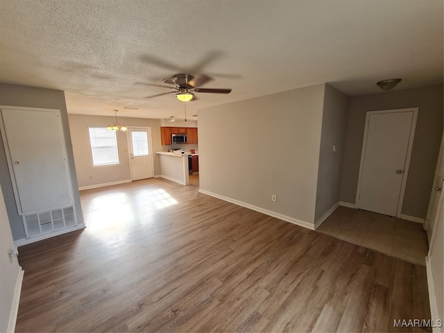 unfurnished living room featuring light wood-type flooring, ceiling fan with notable chandelier, and a textured ceiling