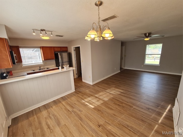 kitchen with ceiling fan with notable chandelier, light wood-type flooring, a textured ceiling, and appliances with stainless steel finishes