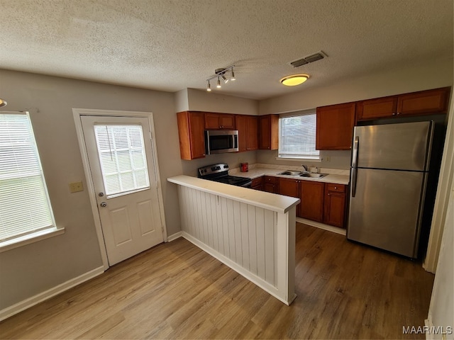 kitchen with light hardwood / wood-style floors, a textured ceiling, sink, kitchen peninsula, and stainless steel appliances