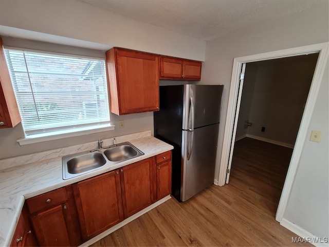 kitchen with a textured ceiling, stainless steel refrigerator, sink, and light hardwood / wood-style flooring