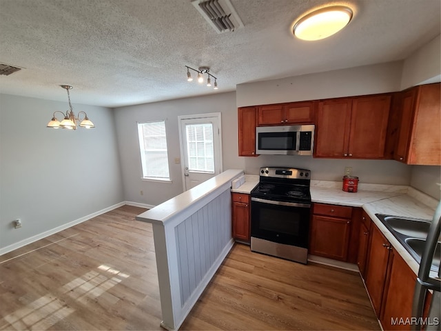 kitchen with a textured ceiling, decorative light fixtures, light hardwood / wood-style flooring, appliances with stainless steel finishes, and an inviting chandelier