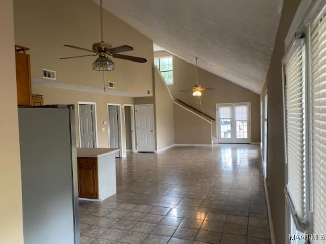 unfurnished living room featuring ceiling fan, a textured ceiling, light tile patterned floors, and high vaulted ceiling