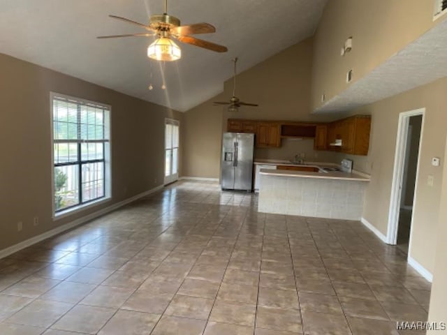 kitchen featuring light tile patterned flooring, high vaulted ceiling, kitchen peninsula, ceiling fan, and stainless steel refrigerator with ice dispenser