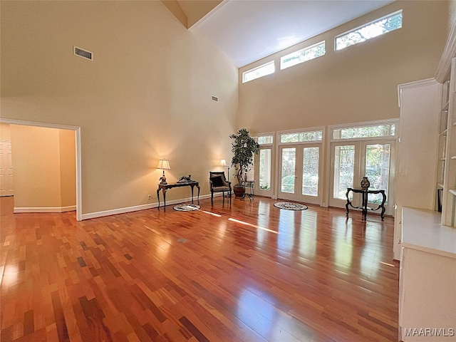 unfurnished living room featuring hardwood / wood-style floors, a towering ceiling, and french doors