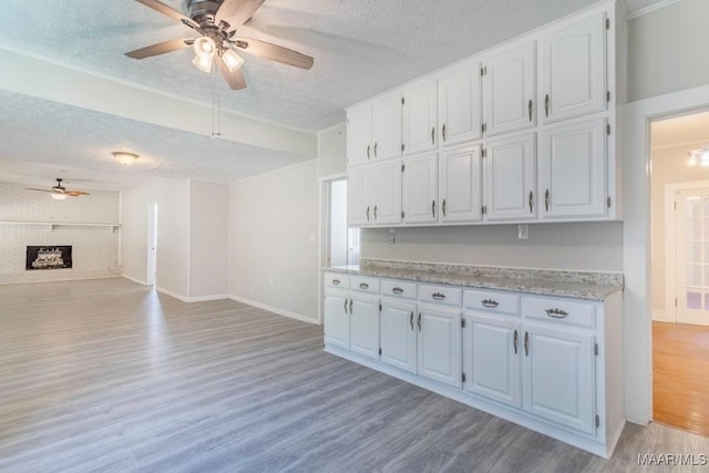 kitchen with white cabinetry, a brick fireplace, a textured ceiling, brick wall, and light hardwood / wood-style floors