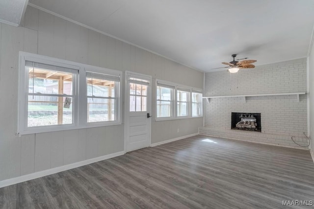 unfurnished living room featuring brick wall, a brick fireplace, ornamental molding, dark hardwood / wood-style flooring, and ceiling fan