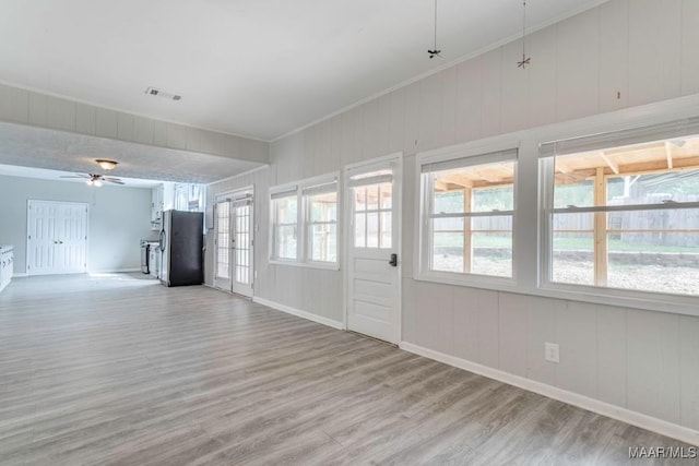 unfurnished living room with crown molding, wood walls, light wood-type flooring, and ceiling fan