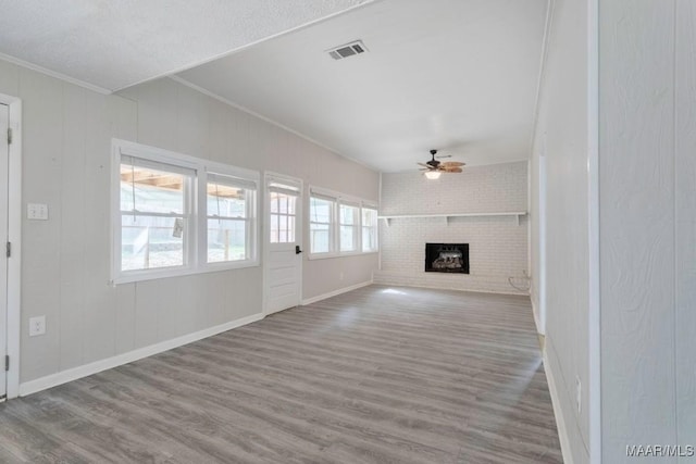 unfurnished living room with crown molding, wood-type flooring, brick wall, a brick fireplace, and ceiling fan