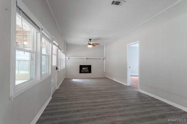 unfurnished living room with brick wall, dark wood-type flooring, ceiling fan, a brick fireplace, and crown molding