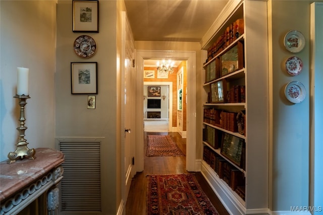 corridor featuring crown molding, dark hardwood / wood-style floors, and a notable chandelier