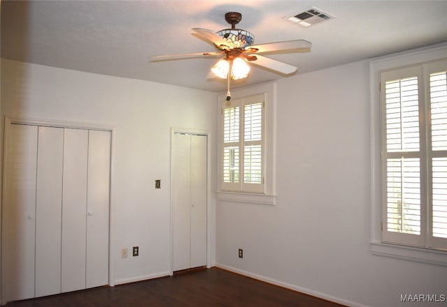 unfurnished bedroom with ceiling fan, two closets, and dark hardwood / wood-style flooring