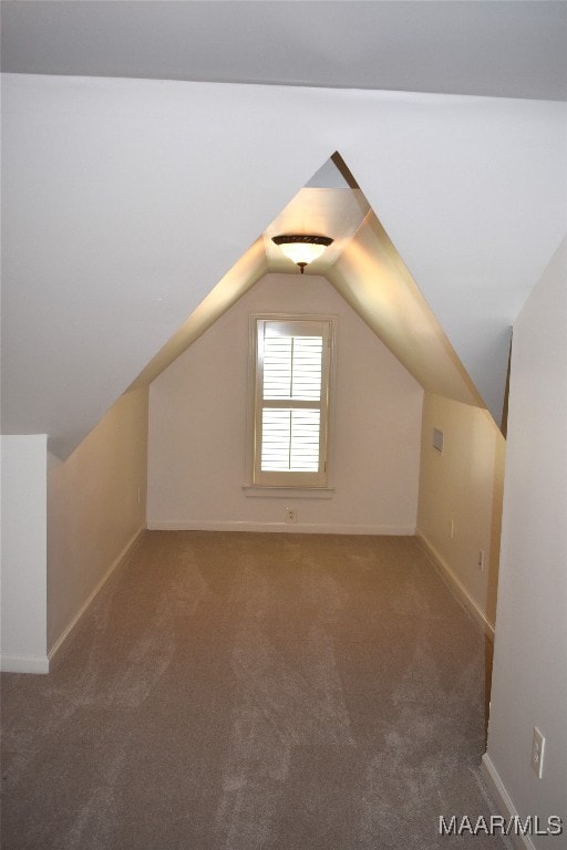 additional living space with dark colored carpet and vaulted ceiling