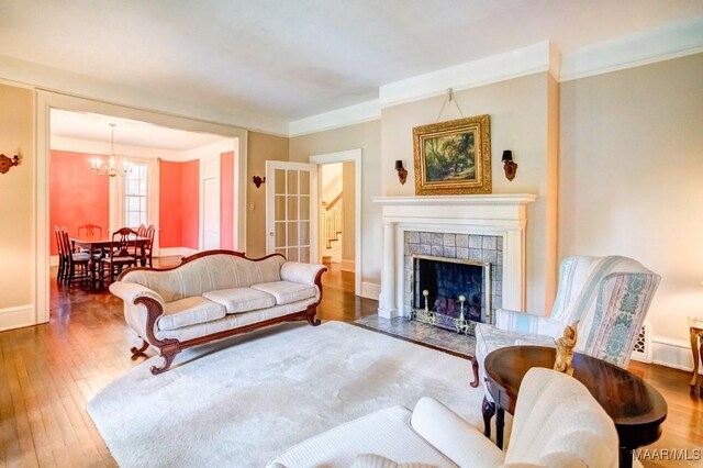 living room with a notable chandelier, a tiled fireplace, hardwood / wood-style flooring, and crown molding