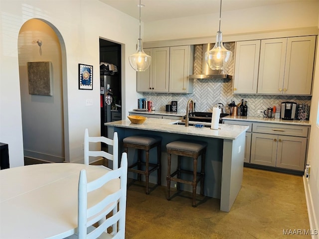 kitchen featuring gray cabinetry, a center island with sink, hanging light fixtures, and decorative backsplash