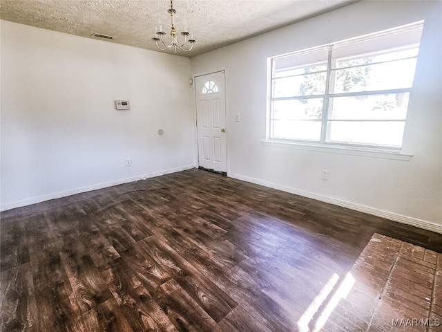 empty room with a textured ceiling, an inviting chandelier, and dark wood-type flooring