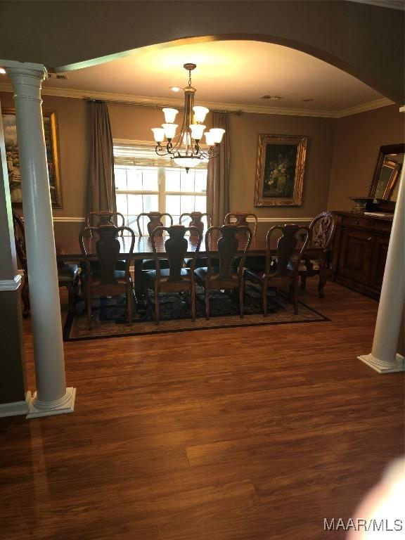 dining space featuring crown molding, decorative columns, an inviting chandelier, and dark wood-type flooring