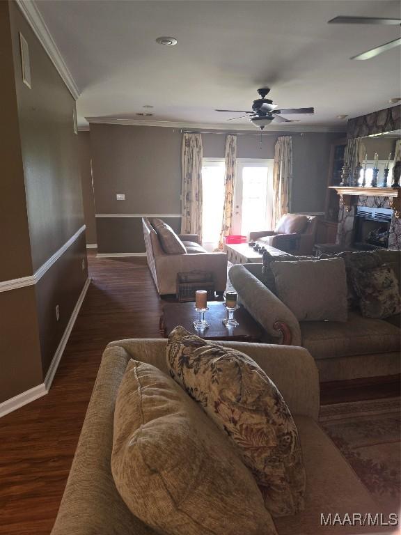 living room with a stone fireplace, ceiling fan, crown molding, and dark hardwood / wood-style flooring