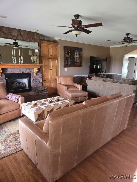 living room with crown molding, ceiling fan, hardwood / wood-style flooring, and a stone fireplace