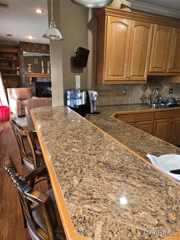 kitchen featuring sink, wood-type flooring, a breakfast bar area, crown molding, and decorative backsplash