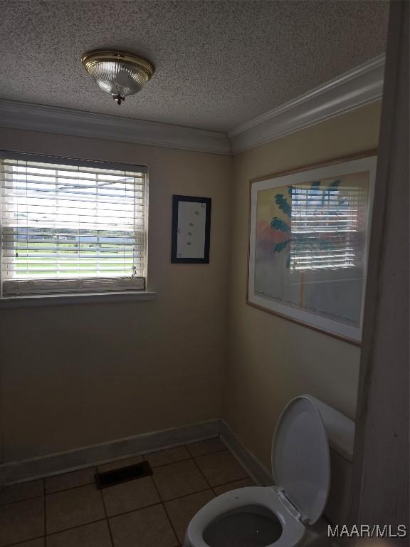 bathroom with a textured ceiling, tile patterned flooring, ornamental molding, and toilet