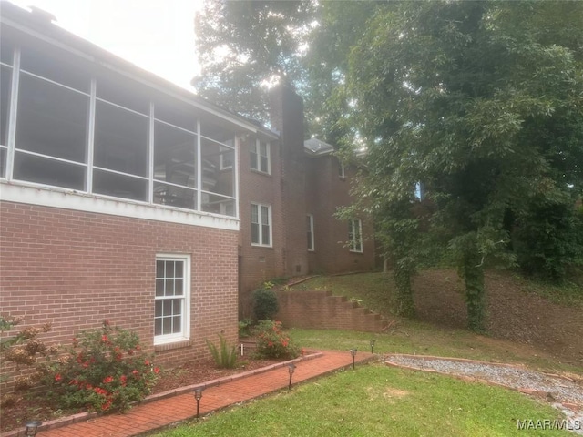 view of property exterior with a sunroom, a lawn, and brick siding