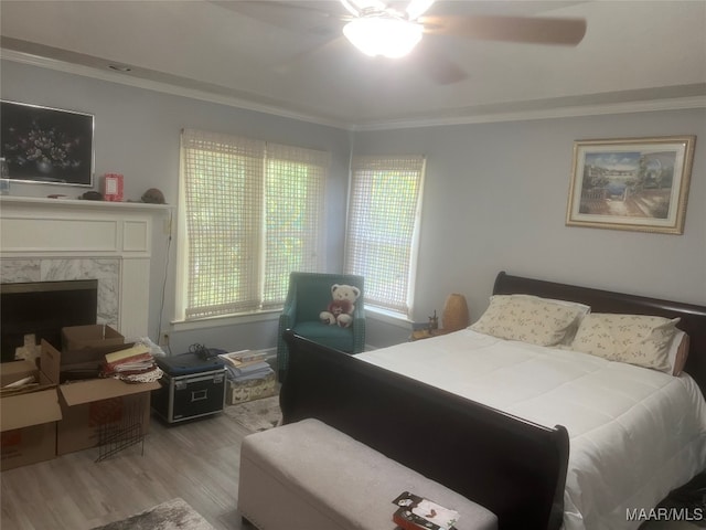 bedroom with ceiling fan, crown molding, light hardwood / wood-style flooring, and a high end fireplace