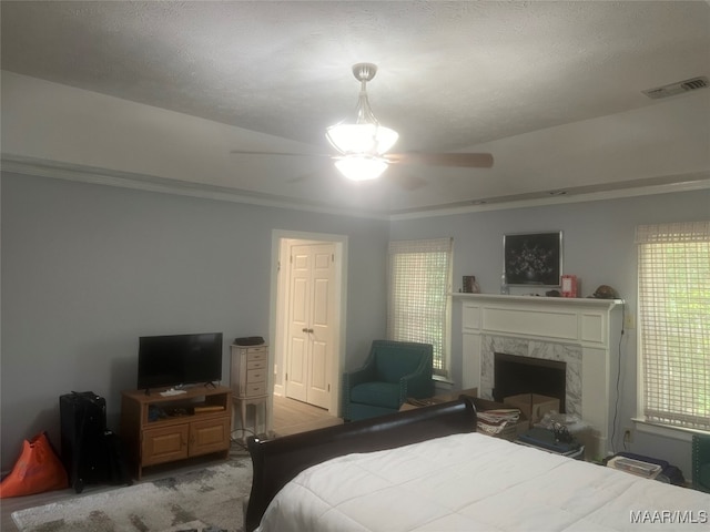 bedroom with a premium fireplace, ornamental molding, a textured ceiling, and ceiling fan