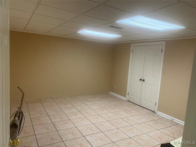 spare room featuring concrete block wall, baseboards, and a drop ceiling