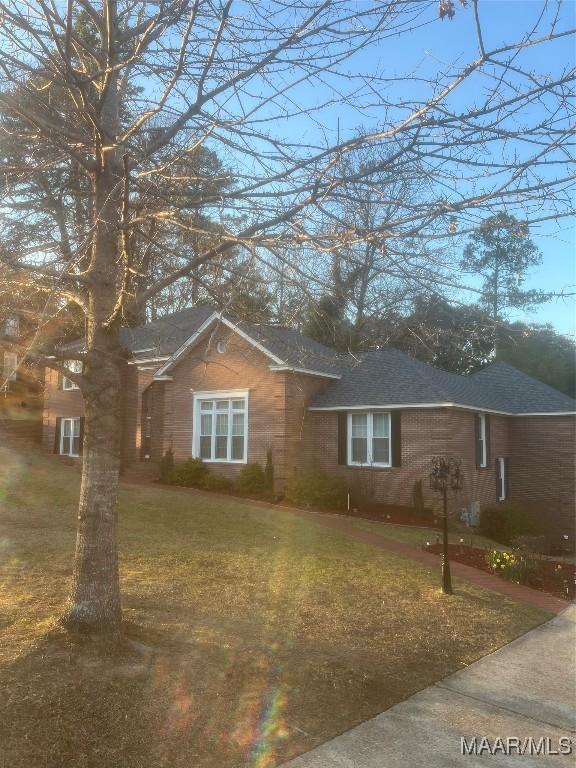 view of front facade featuring a shingled roof, a front lawn, and brick siding