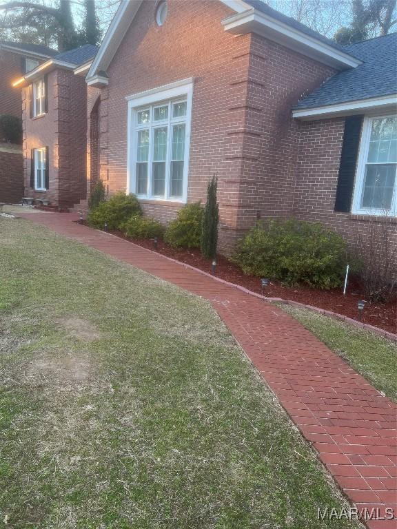 view of side of property with a yard, a shingled roof, and brick siding