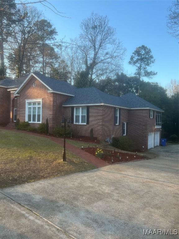 view of front of house featuring driveway, roof with shingles, an attached garage, a front lawn, and brick siding