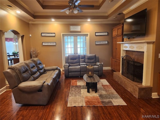 living room with ceiling fan, ornate columns, a tile fireplace, and a tray ceiling