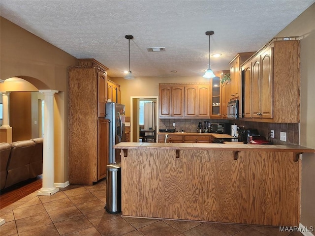 kitchen with kitchen peninsula, a kitchen breakfast bar, ornate columns, stainless steel appliances, and hanging light fixtures