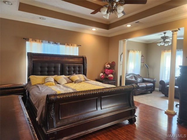 bedroom featuring ceiling fan, a raised ceiling, and decorative columns