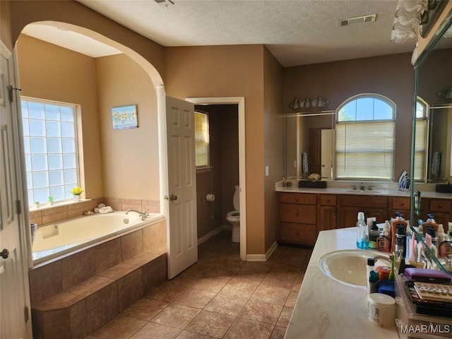 bathroom featuring vanity, a relaxing tiled tub, toilet, and plenty of natural light