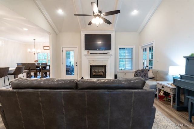 living room with ceiling fan with notable chandelier, a high end fireplace, crown molding, vaulted ceiling, and light hardwood / wood-style flooring