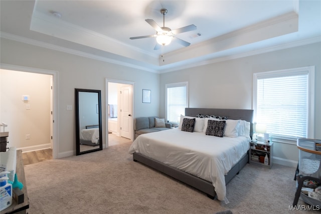 carpeted bedroom with ornamental molding, a tray ceiling, connected bathroom, and ceiling fan