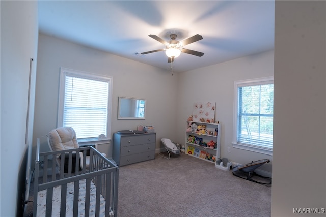 carpeted bedroom with a crib and ceiling fan