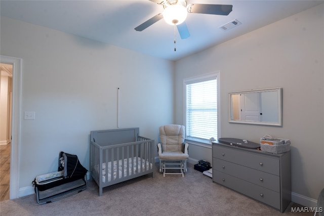 bedroom featuring a crib, light colored carpet, and ceiling fan