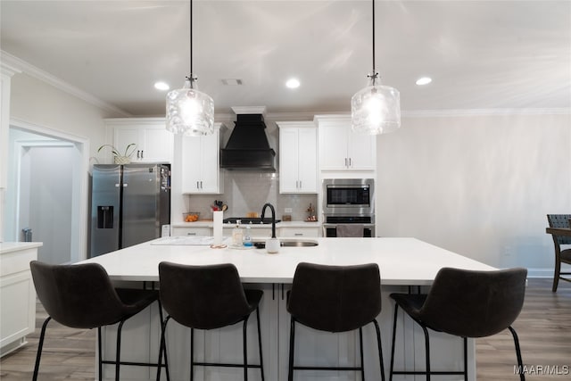 kitchen featuring wood-type flooring, stainless steel appliances, sink, custom exhaust hood, and a center island with sink