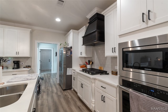 kitchen featuring custom exhaust hood, appliances with stainless steel finishes, light wood-type flooring, and white cabinetry