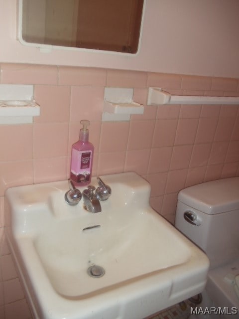 bathroom with toilet, tile walls, and sink