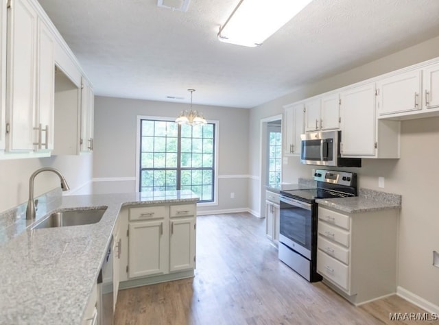 kitchen with light hardwood / wood-style floors, sink, white cabinets, appliances with stainless steel finishes, and decorative light fixtures