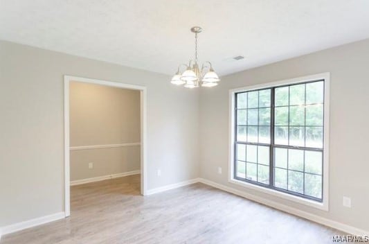 unfurnished room with a healthy amount of sunlight, an inviting chandelier, and light hardwood / wood-style flooring