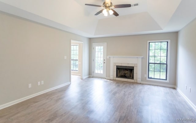 unfurnished living room featuring a raised ceiling, a tiled fireplace, ceiling fan, and light hardwood / wood-style flooring