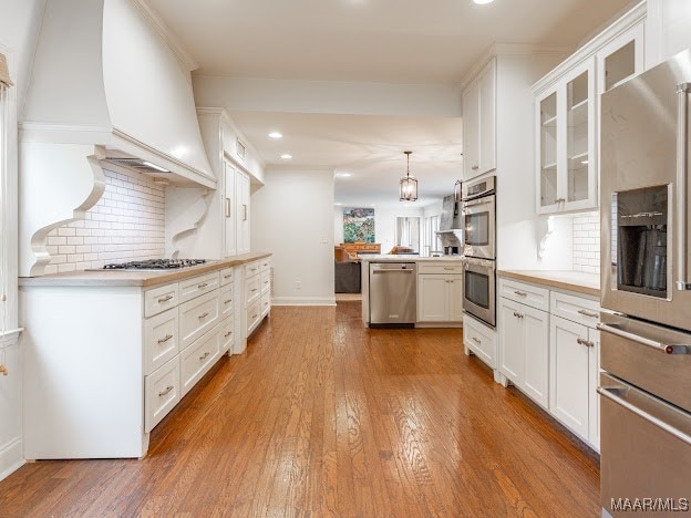 kitchen with decorative backsplash, white cabinets, stainless steel appliances, decorative light fixtures, and hardwood / wood-style floors