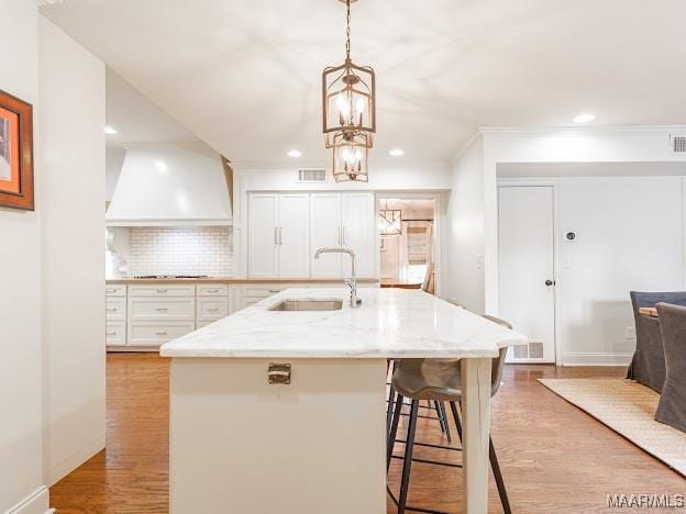 kitchen with white cabinets, a sink, premium range hood, light wood finished floors, and light stone counters