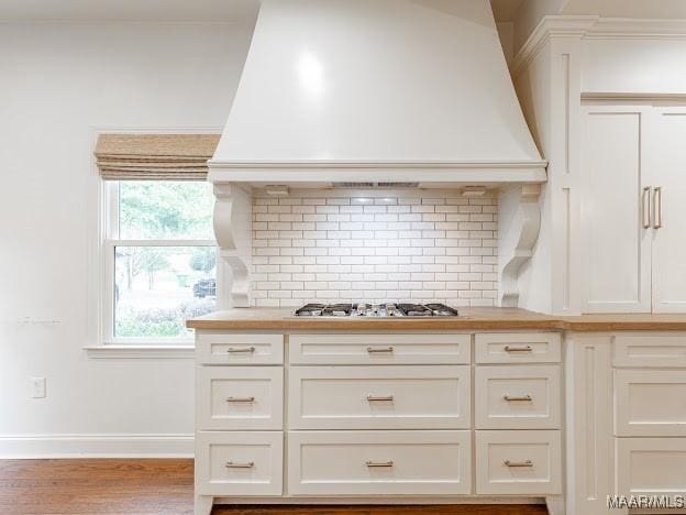 kitchen with custom exhaust hood, tasteful backsplash, baseboards, wood finished floors, and stainless steel gas cooktop