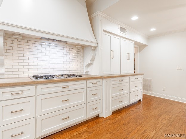 kitchen with premium range hood, tasteful backsplash, stainless steel gas cooktop, white cabinetry, and light wood-type flooring